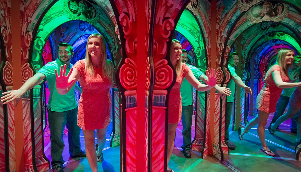 A woman and a man are navigating through a colorful mirror maze with multiple reflections around them