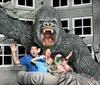 A family poses playfully with a giant gorilla statue that appears to be roaring and grabbing them