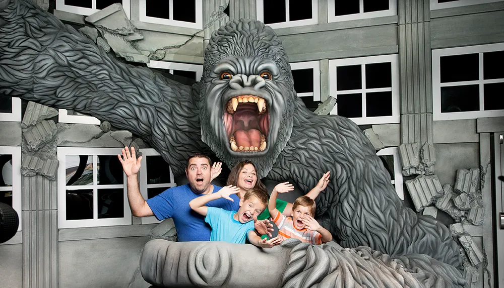 A family poses playfully with a giant gorilla statue that appears to be roaring and grabbing them