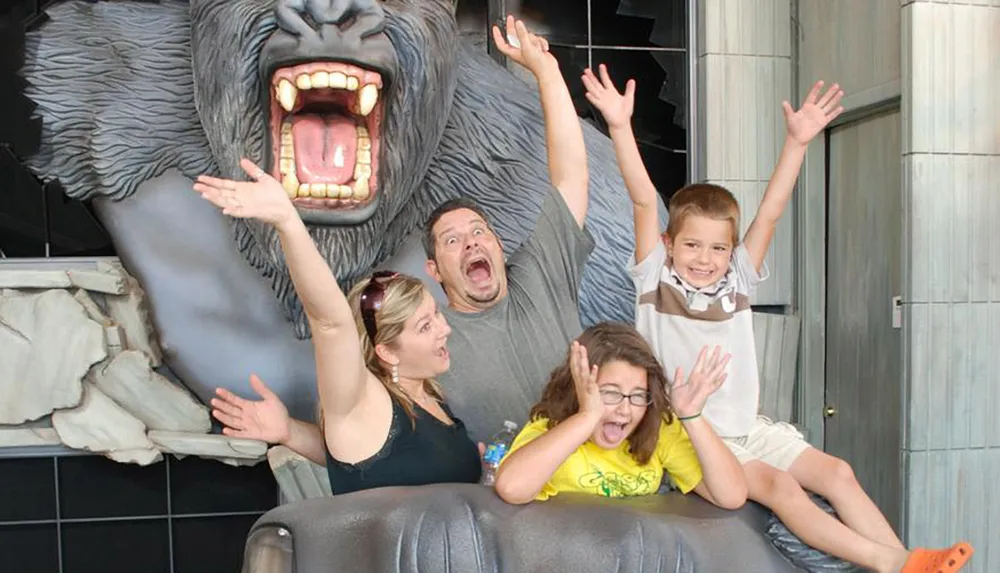 A family is playfully posing with their hands up as if scared in front of a large faux angry gorilla exhibit