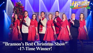 A group of performers in festive attire is on stage in a Christmas-themed show, with a backdrop of falling snow.