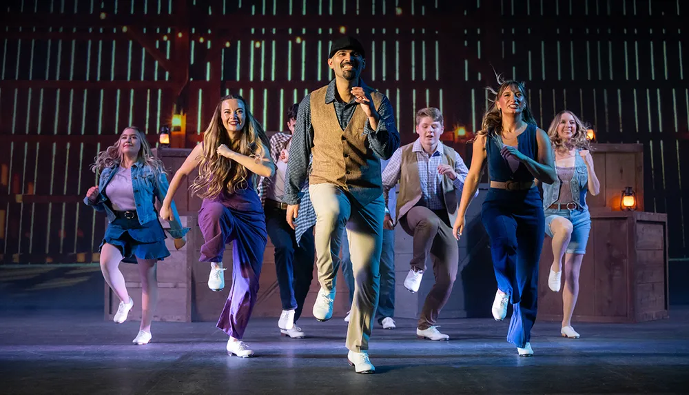 A group of dancers performs energetically on stage all wearing casual attire and tap shoes