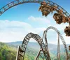 A roller coaster full of riders is ascending a steep loop with a lush green forest in the background