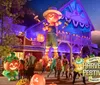 A lively Halloween-themed festival scene features colorful decorations a giant pumpkin figure and people enjoying the festivities under vibrant purple lighting