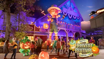 A lively Halloween-themed festival scene features colorful decorations, a giant pumpkin figure, and people enjoying the festivities under vibrant purple lighting.