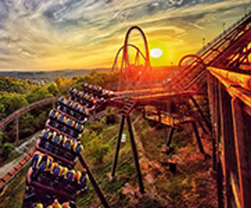 A roller coaster full of passengers is dramatically curving on its track against the backdrop of a vibrant sunset