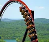 A roller coaster full of riders is ascending a steep loop with a lush green forest in the background
