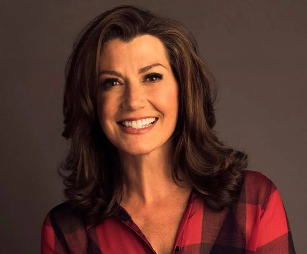 The image shows a woman with shoulder-length hair smiling warmly at the camera wearing a red and black checkered top against a neutral background