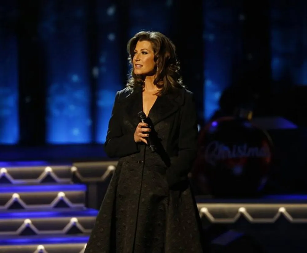 A woman stands on a stage with a microphone possibly performing or preparing to sing with a festive background indicating a Christmas-themed event