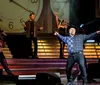 A performer in a cowboy hat is exuberantly singing on stage with musicians and dancers in the background all set against an oversized clock backdrop