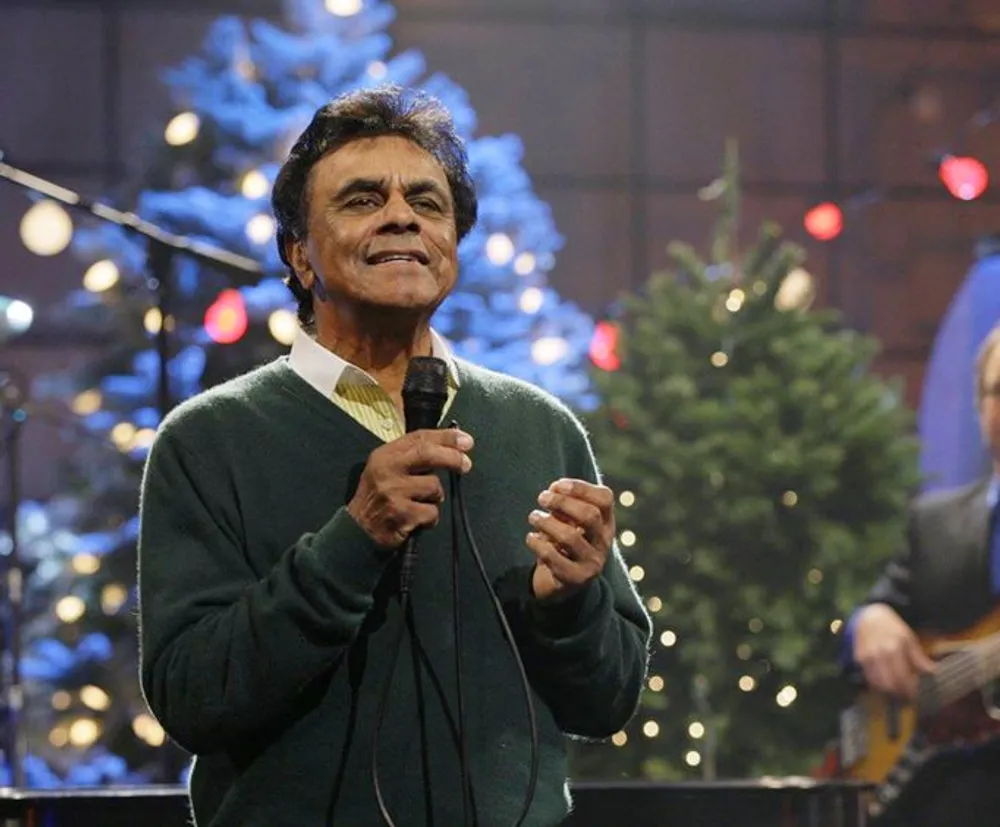A person is performing with a microphone in front of a Christmas tree likely singing a song