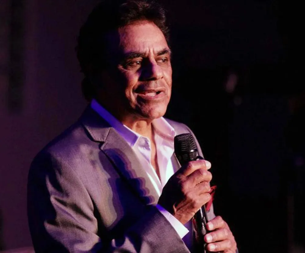A man in a gray suit is holding a microphone presumably addressing an audience or performing