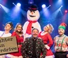 A group of people in festive attire pose with a snowman under stage lights with a sign reading Laughter in Overdrive