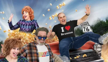 A group of cheerful people in colorful outfits are playfully posed with popcorn and a vintage car against a backdrop of a road sign for Missouri Route 76.