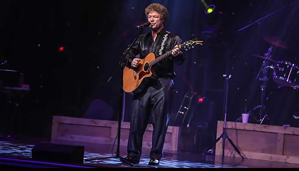 A musician is performing on stage playing an acoustic guitar and singing into a microphone