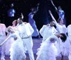 A person in a snowman costume is surrounded by smiling dancers in festive outfits on a winter-themed stage