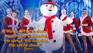 A person in a snowman costume is surrounded by smiling dancers in festive outfits on a winter-themed stage.