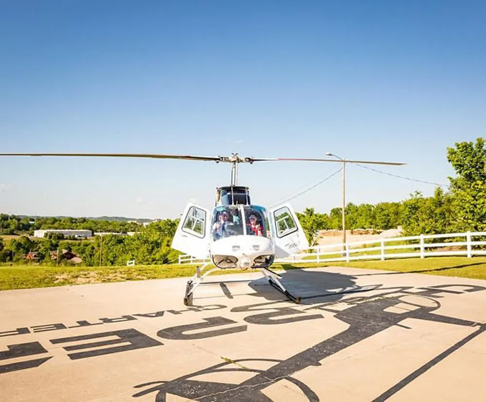 A helicopter with passengers is shown preparing for takeoff or having just landed on a sunny day at a helipad marked with H