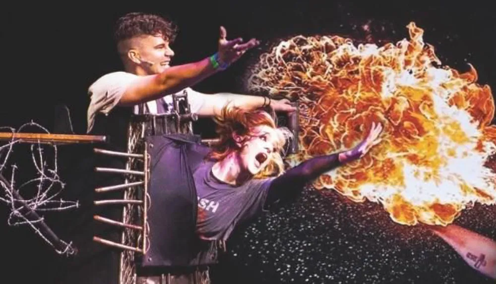 Two performers are on stage with one seemingly pouring fuel creating a dramatic fireball effect around the other