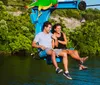 A man and a woman are smiling and enjoying a chairlift ride over a body of water surrounded by lush greenery