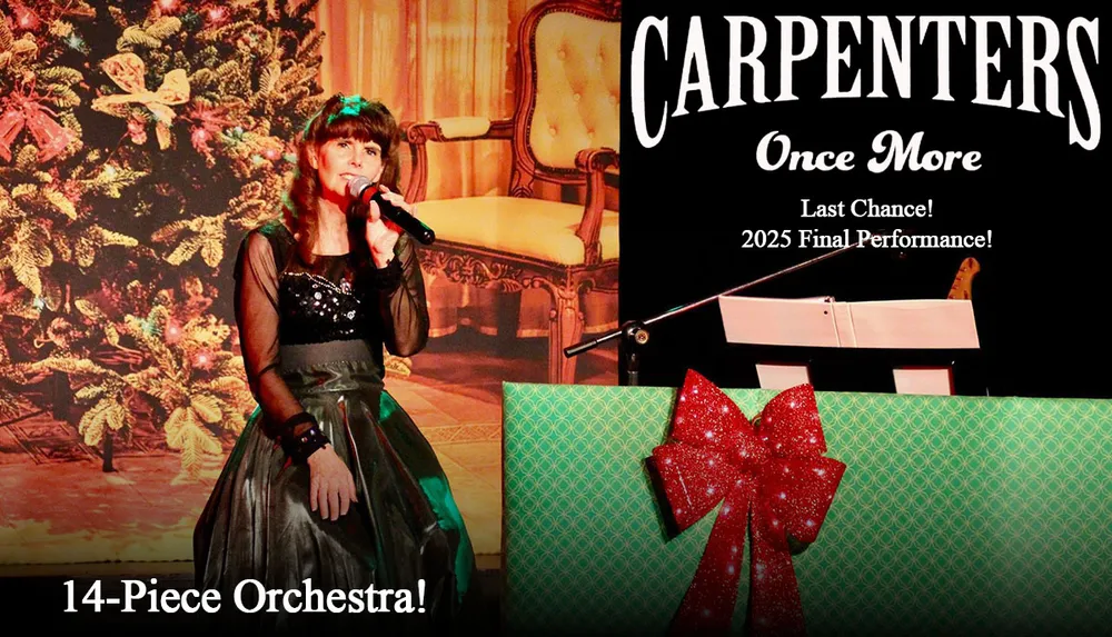 A person is performing on stage with a microphone in hand against a festively decorated backdrop with a Christmas tree and a large gift-wrapped box