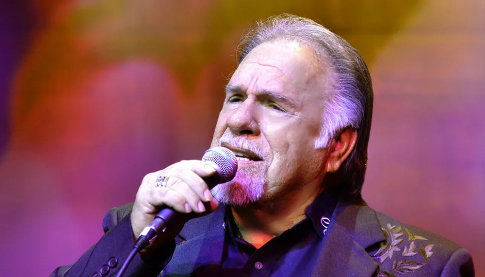 A man is passionately singing into a microphone on a colorful stage