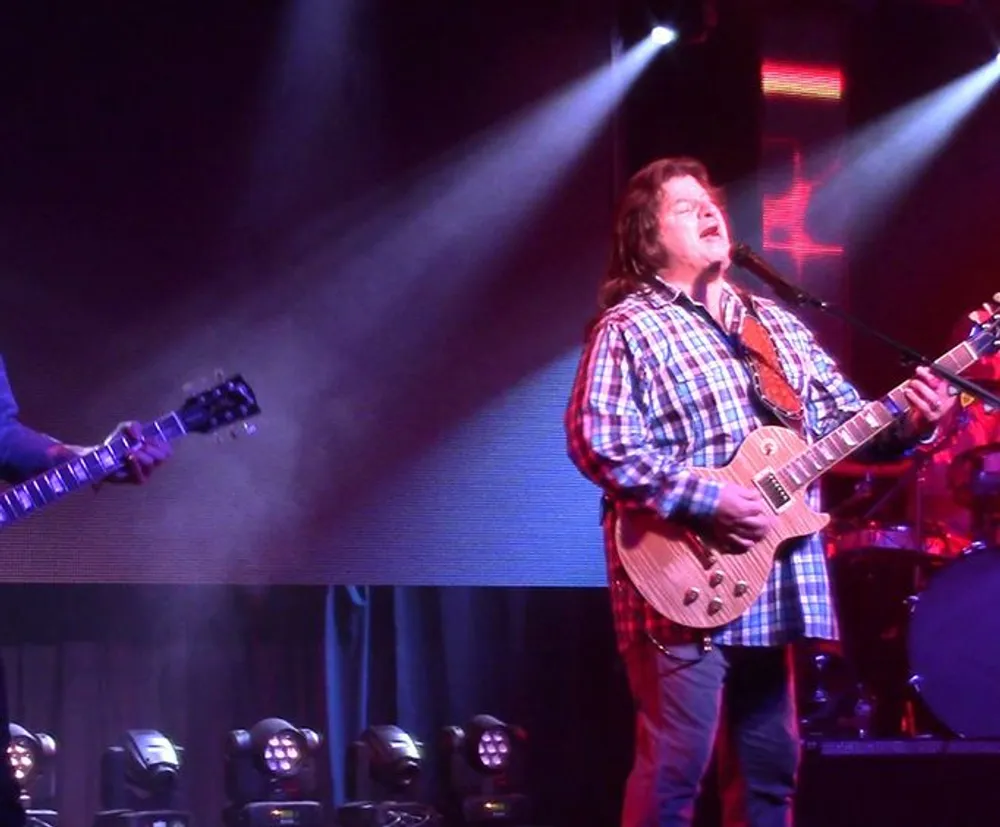 A musician is playing an electric guitar and singing on stage under a spotlight