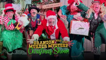 Four people are dressed in colorful and theatrical Christmas-themed costumes, expressing exaggerated emotions in what appears to be a festive play or performance.