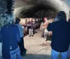 A group of people are attentively listening to a speaker during a tour in a wine cellar lined with barrels