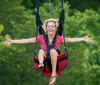 A person is joyfully zip-lining with arms outstretched against a backdrop of lush green trees