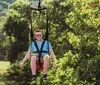 A person is joyfully zip-lining with arms outstretched against a backdrop of lush green trees