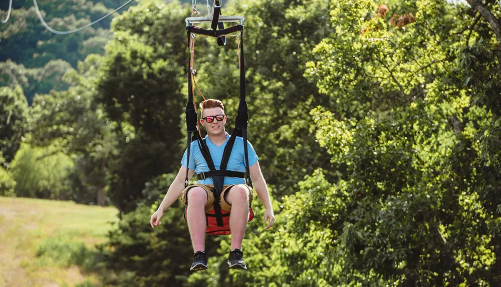 A person is enjoying a ride on a zip line through a lush forested area wearing a harness and sunglasses