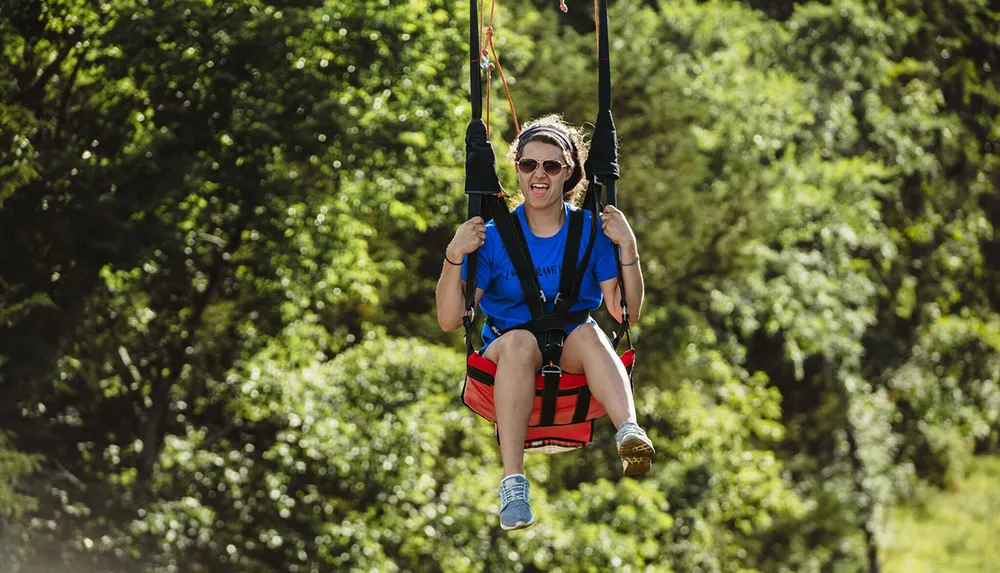 A person in a blue shirt is joyfully ziplining through a lush green forest