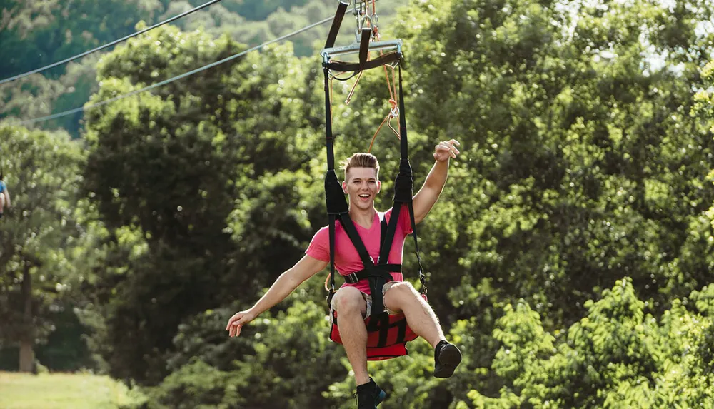 A person is joyfully riding a zipline through a lush green forest