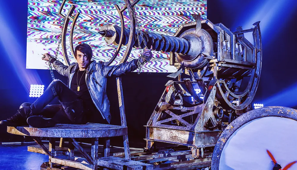 A person is chained to a large industrial-looking machine with a dramatic background and lighting