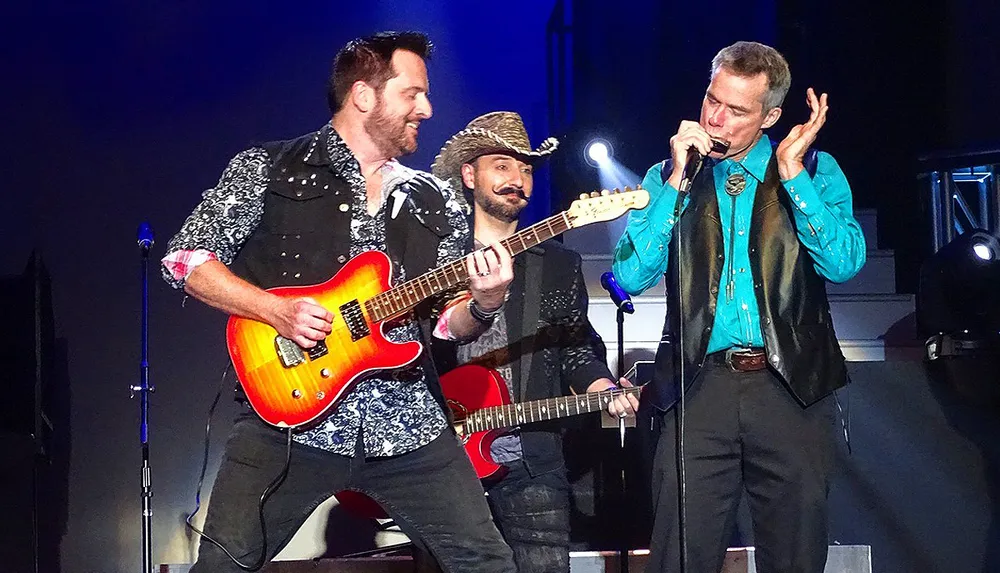 Three musicians are performing on stage with two playing guitars and one playing a harmonica