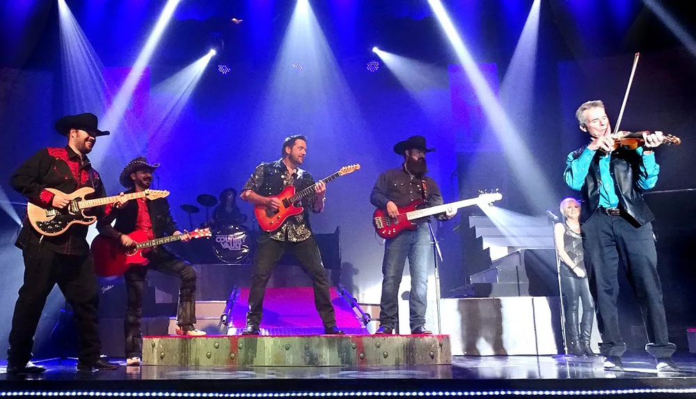 A band performs energetically on stage featuring guitarists and a violinist under dramatic lighting