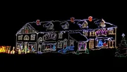 This image shows a house elaborately decorated with colorful Christmas lights, featuring outlines of the architecture and festive motifs such as the word 