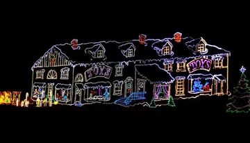 This image shows a house elaborately decorated with colorful Christmas lights, featuring outlines of the architecture and festive motifs such as the word 