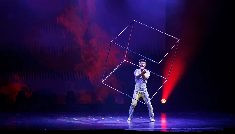 A performer on stage manipulates an intricate geometric shape under dramatic red and blue stage lighting