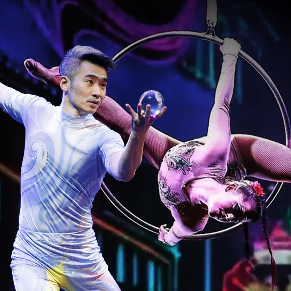 The image features a man skillfully manipulating a crystal ball and a female acrobat elegantly posed on a hoop against a vibrant background