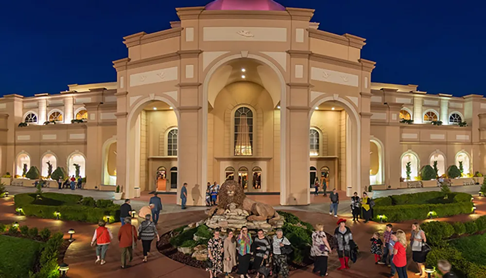 The image shows people walking near an elegant building with a dome and arches illuminated in the evening