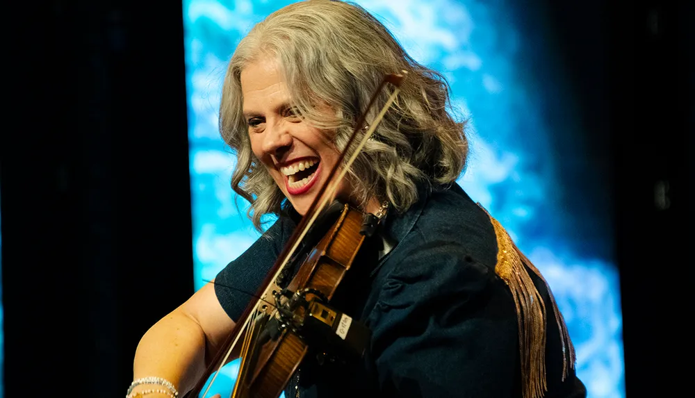 A woman with gray hair is joyfully playing the violin on stage