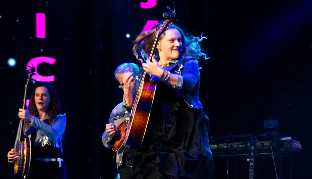 The image shows a lively performance with three musicians on stage one playing a guitar energetically