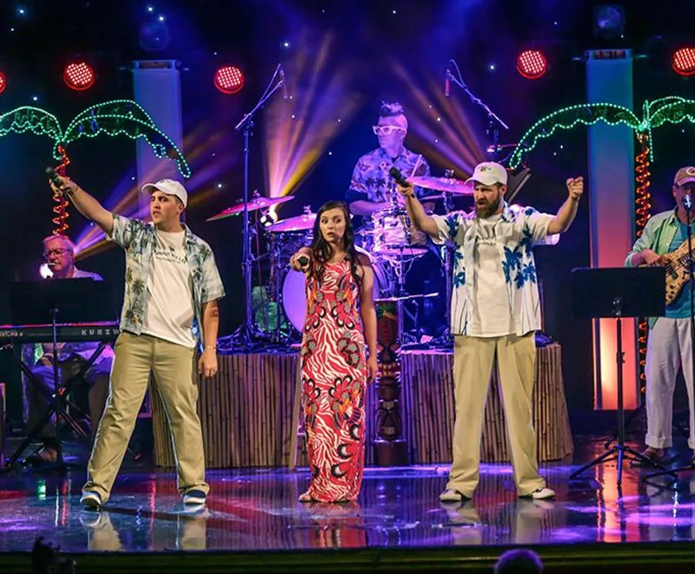 The image shows a vibrant live music performance with a band playing in the background and three singers in the foreground on stage under colorful lighting