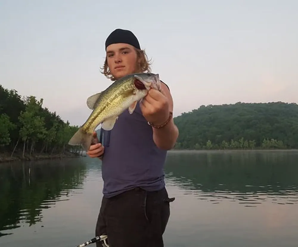 A person is holding a fish with a lake and treeline in the background during dusk