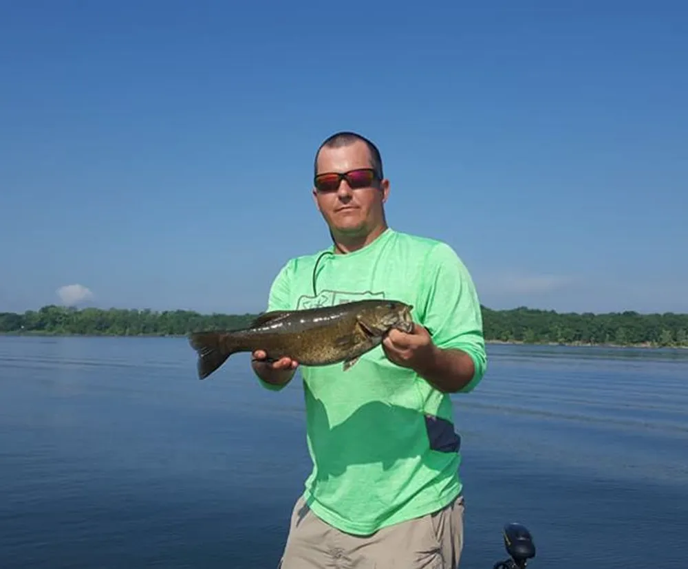 A person is holding a fish with a lake and treeline in the background