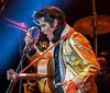 A performer in a gold jacket passionately sings into a vintage microphone on stage with a guitar slung across their shoulder