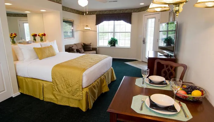 This image shows a neatly arranged hotel or guest room with a double bed dining setup for two and a small living area in the background