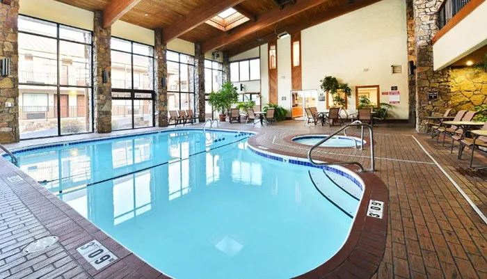 This image shows an indoor swimming pool area with lounge chairs large windows and a hot tub reflecting a leisurely and comfortable atmosphere